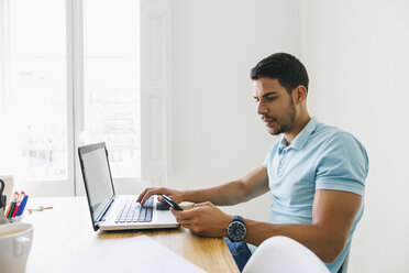 Junger Mann arbeitet im Büro und benutzt einen Laptop - EBSF001494