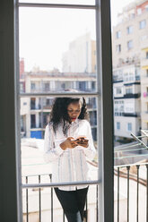 Junge Geschäftsfrau steht auf einem Balkon und prüft Nachrichten auf ihrem Smartphone - EBSF001521