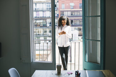 Junge Geschäftsfrau steht auf einem Balkon und prüft Nachrichten auf ihrem Smartphone - EBSF001522