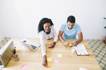 Young man and woman in office writing on adhesive notes on desk - EBSF001534