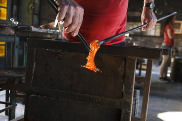 Mann bei der Arbeit mit geschmolzenem Glas mit einer Pinzette in einer Glasfabrik - ABZF000662