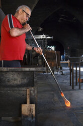 Mann bläst mit einem Rohr geschmolzenes Glas in einer Glasfabrik - ABZF000664