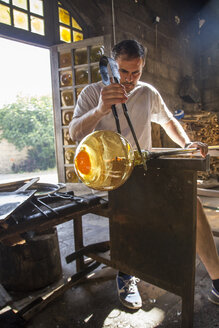 Mann bei der Arbeit mit geschmolzenem Glas mit einer Pinzette in einer Glasfabrik - ABZF000671
