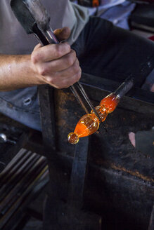 Mann bei der Arbeit mit geschmolzenem Glas mit einer Pinzette in einer Glasfabrik - ABZF000672