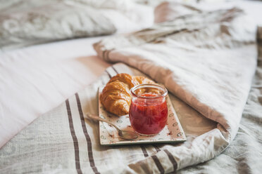 Teller mit Croissant und Glas Erdbeermarmelade auf dem Bett - ASCF000623