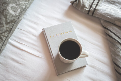 Buch und eine Tasse schwarzer Kaffee auf einem Bett - ASCF000624
