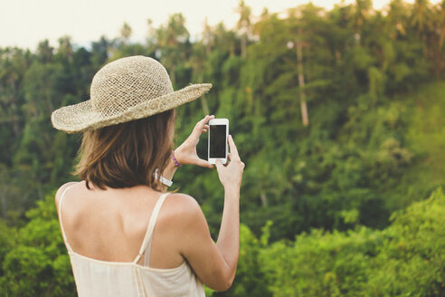 Rückansicht einer Frau, die ein Foto mit ihrem Smartphone in der Natur macht - KNTF000348