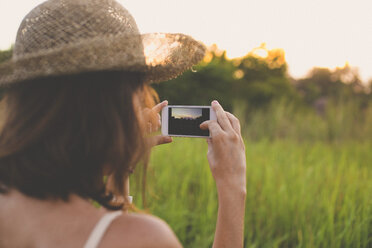 Rückansicht einer Frau, die ein Foto mit ihrem Smartphone in der Natur macht - KNTF000349