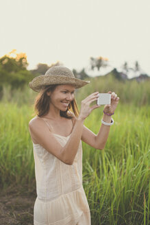 Lächelnde Frau beim Fotografieren mit Smartphone in der Natur - KNTF000351