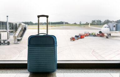 Suitcase at the airport, passenger airplane and luggage vehicle in the background - MGOF001951