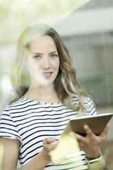 Porträt einer lächelnden Frau mit digitalem Tablet hinter einer Fensterscheibe - SBOF000077