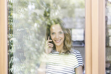 Porträt einer lächelnden Frau am Mobiltelefon hinter einer Fensterscheibe - SBOF000078