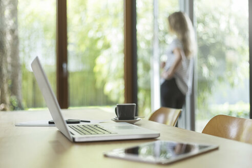 Laptop und digitales Tablet auf einem Tisch mit einer Frau im Hintergrund - SBOF000083