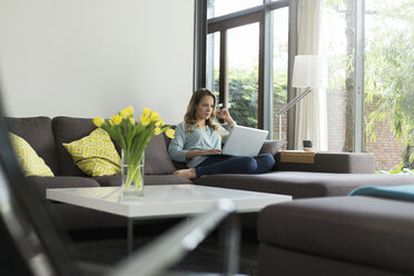 Frau zu Hause auf der Couch sitzend mit Laptop - SBOF000091