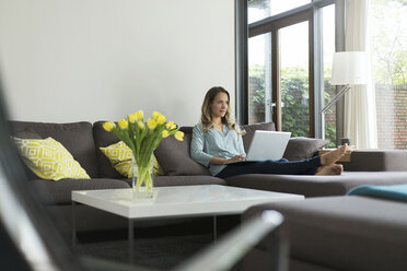 Woman at home sitting on couch using laptop - SBOF000092