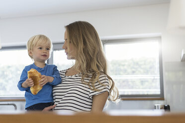 Mother holding son eating croissant - SBOF000105