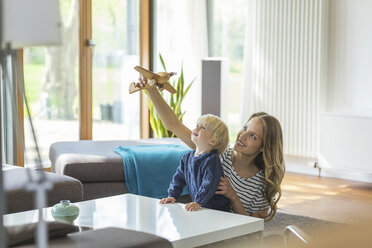 Mother and son playing with toy plane in living room - SBOF000118