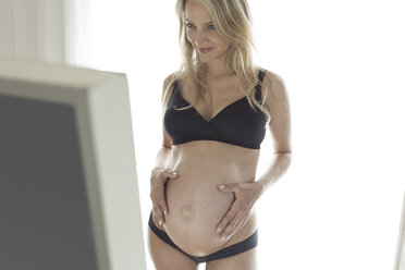 Pregnant woman in bra and panties holding stomach Stock Photo