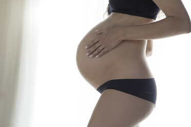 Beautiful pregnant woman in bra and panties holding stomach stock photo