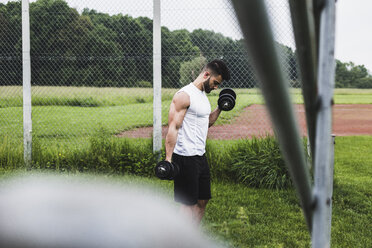 Sportler beim Training mit Hanteln auf einem Sportplatz - UUF007693