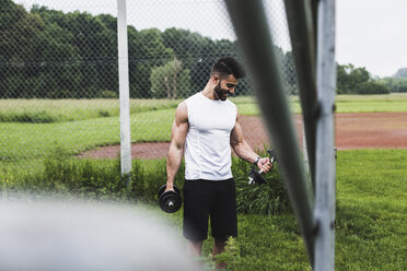 Sportler beim Training mit Hanteln auf einem Sportplatz - UUF007694