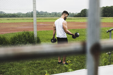 Athlete exercising with dumbbells on sports field - UUF007695