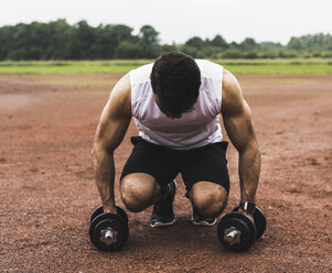 Athlete crouching with dumbbells on sports field - UUF007706