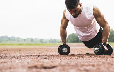 Athlete doing pushups with dumbbells on sports field - UUF007708