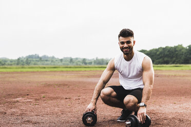 Portrait of smiling athlete with dumbbells on sports field - UUF007709