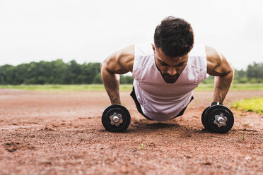 Athlete doing pushups with dumbbells on sports field - UUF007713