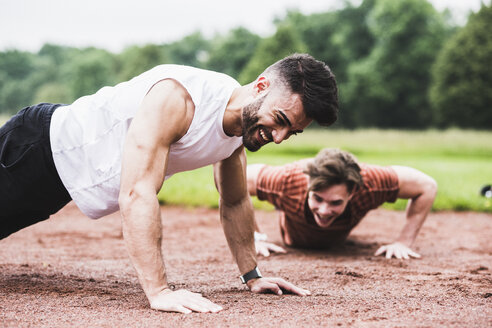 Zwei Sportler machen Liegestütze auf einem Sportplatz - UUF007716