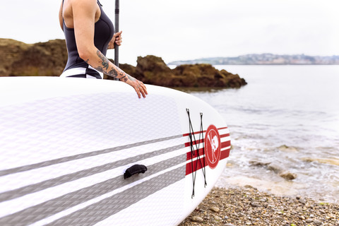 Frau mit Stand Up Paddle Board an der Küste, lizenzfreies Stockfoto