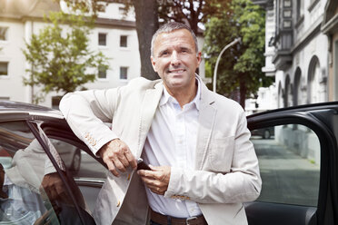 Portrait of smiling man leaning at open car door with car keys - MFF003005