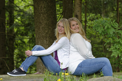 Slim and overweight woman sitting back to back at forest edge - LBF001430