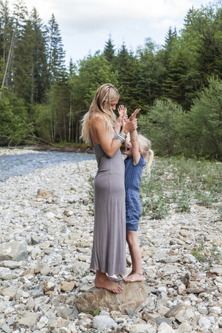 Mutter und ihre kleine Tochter stehen zusammen auf einem Felsen am Flussufer, lizenzfreies Stockfoto
