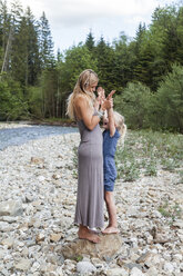 Mutter und ihre kleine Tochter stehen zusammen auf einem Felsen am Flussufer - TCF004997