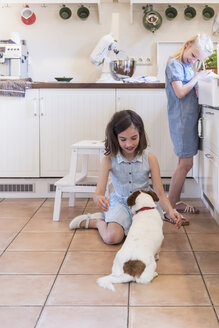 Zwei kleine Mädchen mit ihrem Hund in der Küche - MJF001824