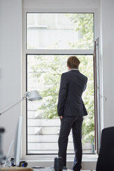 Rückenansicht eines Geschäftsmannes in seinem Büro, der mit seinem Smartphone telefoniert und durch ein offenes Fenster schaut - RHF001598