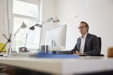 Geschäftsmann sitzt am Schreibtisch in einem Büro und arbeitet mit einem Computer - RHF001620