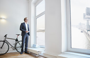 Businessman with smartphone looking through window - RHF001623