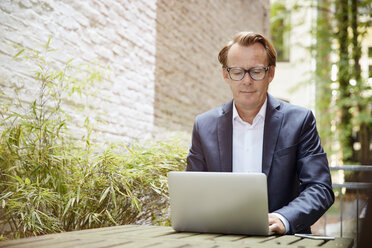 Geschäftsmann sitzt am Tisch in einem Hinterhof und arbeitet mit einem Laptop - RHF001627