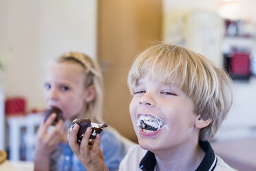 Glücklicher Junge am Tisch, der einen Marshmallow aus Schokolade isst - MJF001836