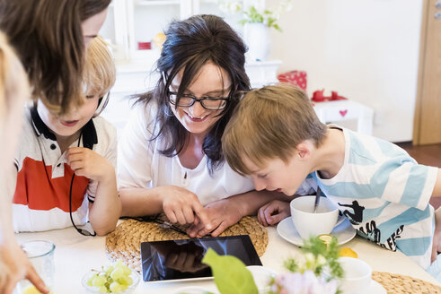 Mutter und drei Kinder teilen sich ein digitales Tablet - MJF001870