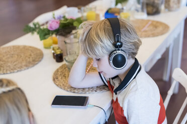 Junge mit Handy und Kopfhörer am Tisch - MJF001885