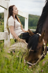 Young woman with brown horse having a break on paddock - MIDF000734