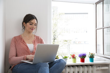 Junge Frau mit Laptop am Fenster - FKF001850