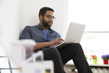 Young man using laptop at the window - FKF001853