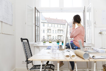 Woman in office sitting on table telephoning - FKF001856