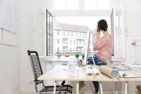 Frau im Büro sitzt auf dem Tisch und telefoniert - FKF001856