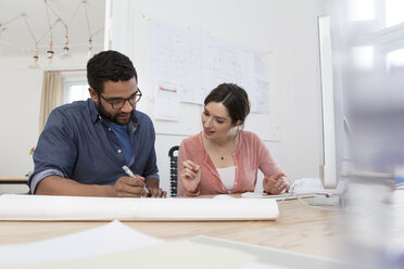 Man and woman discussing at desk in office - FKF001861